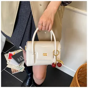 Detail of cream vintage crossbody bag with golden logo and a decorative cherry pendant