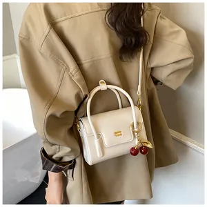 Detail of cream crossbody bag with gold metal logo and decorative red cherry pendant