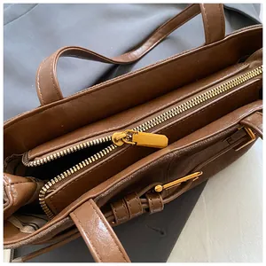 Détail de la fermeture éclair dorée et du cuir marron texturé sur un sac cabas