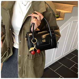 Close-up of black glossy mini handbag with gold logo and red cherry charm accessory