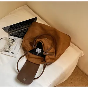 Brown frosted leather tote bag with lifestyle props including headphones and a book