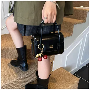 Detail of black patent leather handbag with cherry pendant and golden metal logo