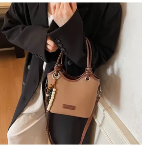 Détail du sac seau en toile marron avec finitions en cuir et breloque perlée élégante