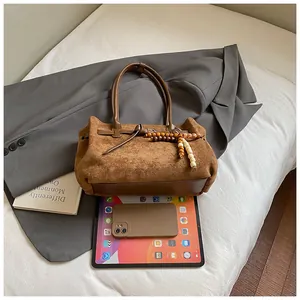 Detail der braunen Wildleder-Tragetasche mit bunten Holzperlen auf einem Business-Blazer