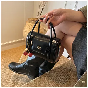 Glossy black leather handbag featuring a red cherry charm and golden logo detail