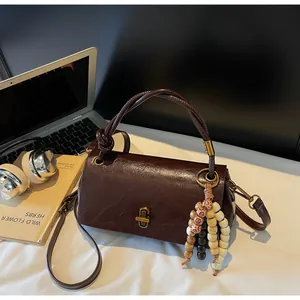 Detail of vintage brown leather bag featuring metallic lock and beaded tassel charm