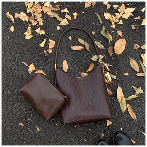 Détail d'un ensemble de sacs en cuir marron foncé avec texture tressée sur feuilles d'automne