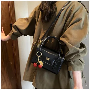 Close-up of black glossy mini square bag with gold logo and cherry pendant detail