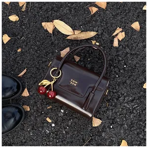 Detail of a chocolate brown patent leather handbag with a red cherry charm on autumn leaves