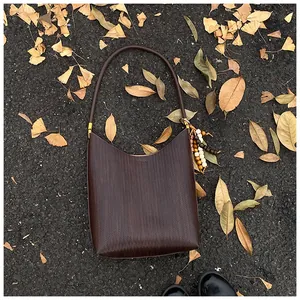 Détail d'un sac à bandoulière tressé marron foncé avec breloque en perles sur feuilles