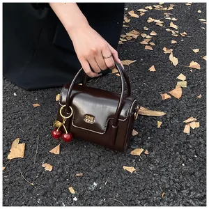 Close-up of retro dark brown patent leather handbag with cherry charm on autumn leaf ground