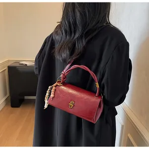 Close-up of dark red crossbody bag with bronze twist lock and ethnic beaded pendant