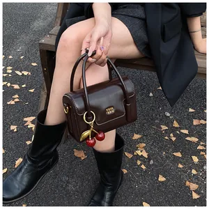 Detail of dark brown glossy leather handbag with a red cherry charm and gold metal logo