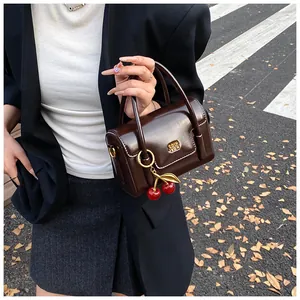 Detail of dark brown retro leather handbag with glossy finish and cherry charm accessory