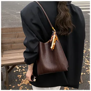 Gros plan du sac seau marron en cuir tressé avec pendentif en perles de bois dans la rue
