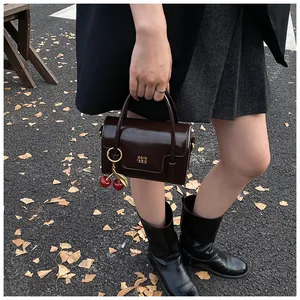 Detail of dark brown leather handbag with metallic cherry charm and gold lettering logo