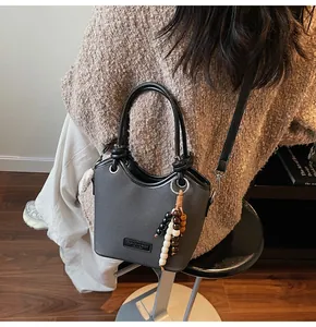Détail du sac seau en cuir gris avec bordures contrastées et breloque en perles