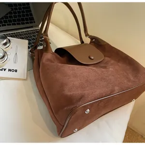 Close-up of brown suede tote bag featuring protective metal bottom studs and soft texture
