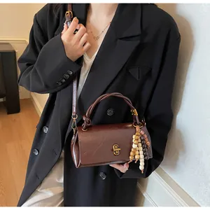 Detail of dark brown leather handbag with gold twist lock and wooden bead pendant
