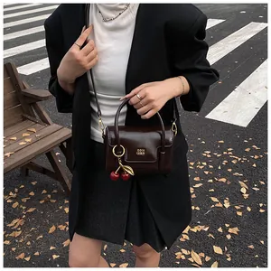Detail of dark brown glossy patent leather bag with gold cherry charm and logo