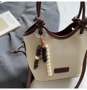 Gros plan d'un sac seau en toile beige avec bordure en cuir marron et breloque en perles