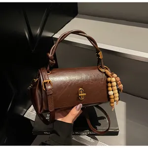 Detail of vintage brown leather cylinder bag with gold clasp and ethnic bead charm