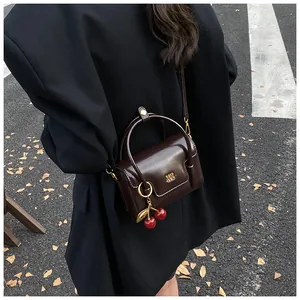Detail of dark brown leather mini bag with gold buckle and cherry charm on black blazer