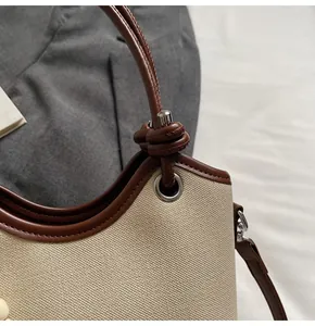 Détail du sac seau en toile montrant la poignée en cuir marron et l'œillet métallique