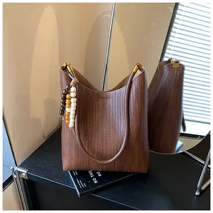 Détail d'un sac cabas tissé marron avec charme en perles colorées et garnitures dorées