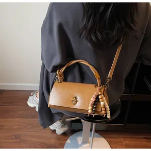 Detail of camel brown crossbody bag featuring golden H-lock and beaded charm decoration