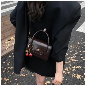 Detail of dark brown glossy leather handbag with gold logo and red cherry charm on strap