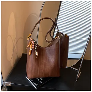 Vue détaillée du sac seau tressé marron foncé avec pompon en perles sur surface sombre