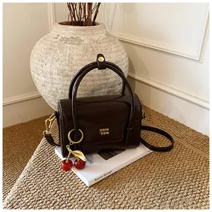 Detail of dark brown glossy handbag with cherry charm and gold branding on woven rug