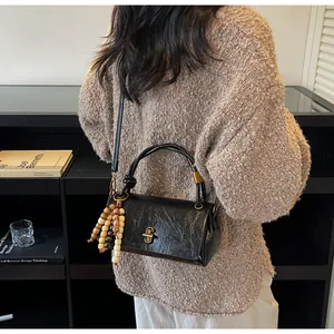 Detail of a black wrinkled leather crossbody bag with wooden bead charm and gold twist lock