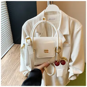 Detail of a creamy white handbag with gold hardware and a cute cherry charm pendant