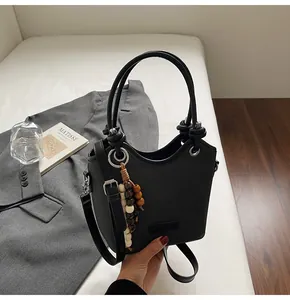 Détail du sac seau noir avec texture de litchi et pendentif décoratif en perles de bois