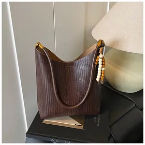 Gros plan d'un sac cabas tissé marron foncé avec anses en cuir et pompon en bois