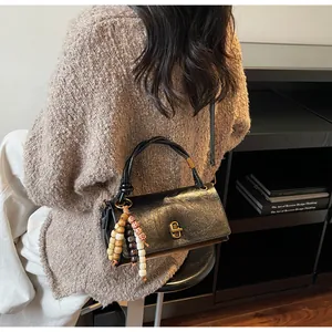 Detailed view of black textured handbag with gold twist lock and ethnic beaded charm detail