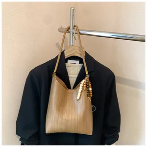 Détail de la texture tressée marron et du pendentif en perles de bois sur le sac hobo