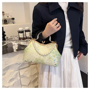 Detail of floral embroidery on a shell-shaped bag with pearl handle and gold chain strap