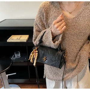 Detail of black textured leather bag with gold hardware and colorful beaded tassel charm