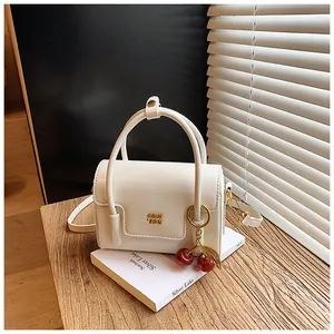 Detailed view of white square handbag with golden logo and a red cherry charm decoration