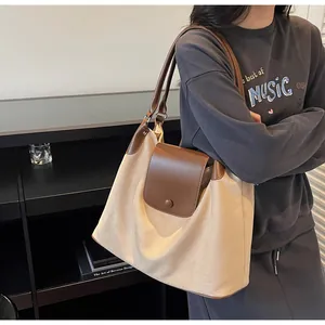 Detail view of large matte canvas tote bag with brown leather handles on shoulder