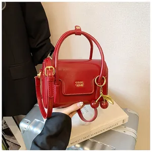 Detail of red patent leather mini bag with cherry charm and gold metal logo on top