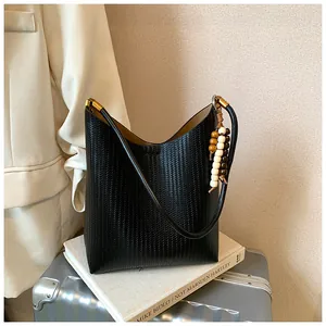 Gros plan d'un sac à bandoulière en cuir tressé noir avec breloque perlée décorative