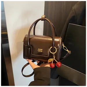 Close-up of chocolate brown square handbag with gold logo and red sequin cherry charm