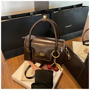 Detail of dark brown glossy leather handbag with gold letters and cherry charm
