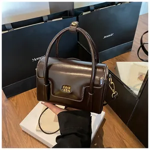 Close-up of a small dark brown glossy leather handbag with gold metal logo and strap