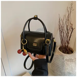 Detail of glossy black leather square bag with gold logo and red cherry pendant