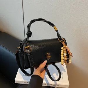 Glossy black leather shoulder bag with knot handle, gold buckle and wooden beaded tassel